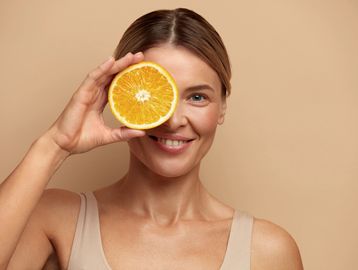 Woman holding half an orange in front of her eye.