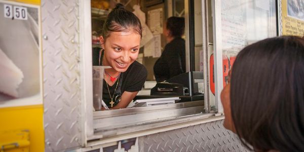 Smiling woman serving customer at food truck window.