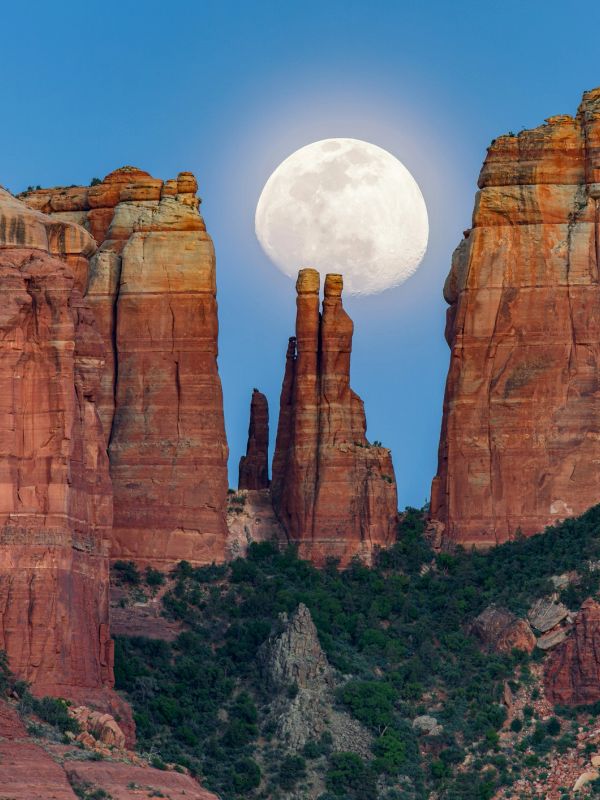 Full moon rising between red rock formations at dusk.