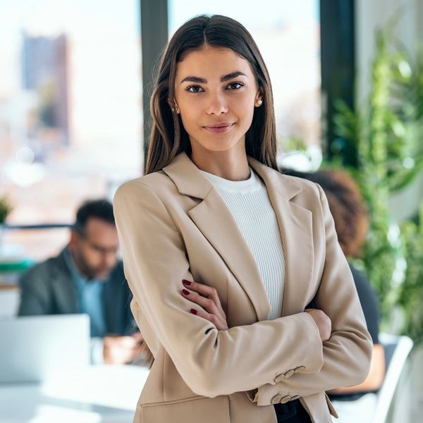 Confident woman in a beige blazer standing in a bright office.