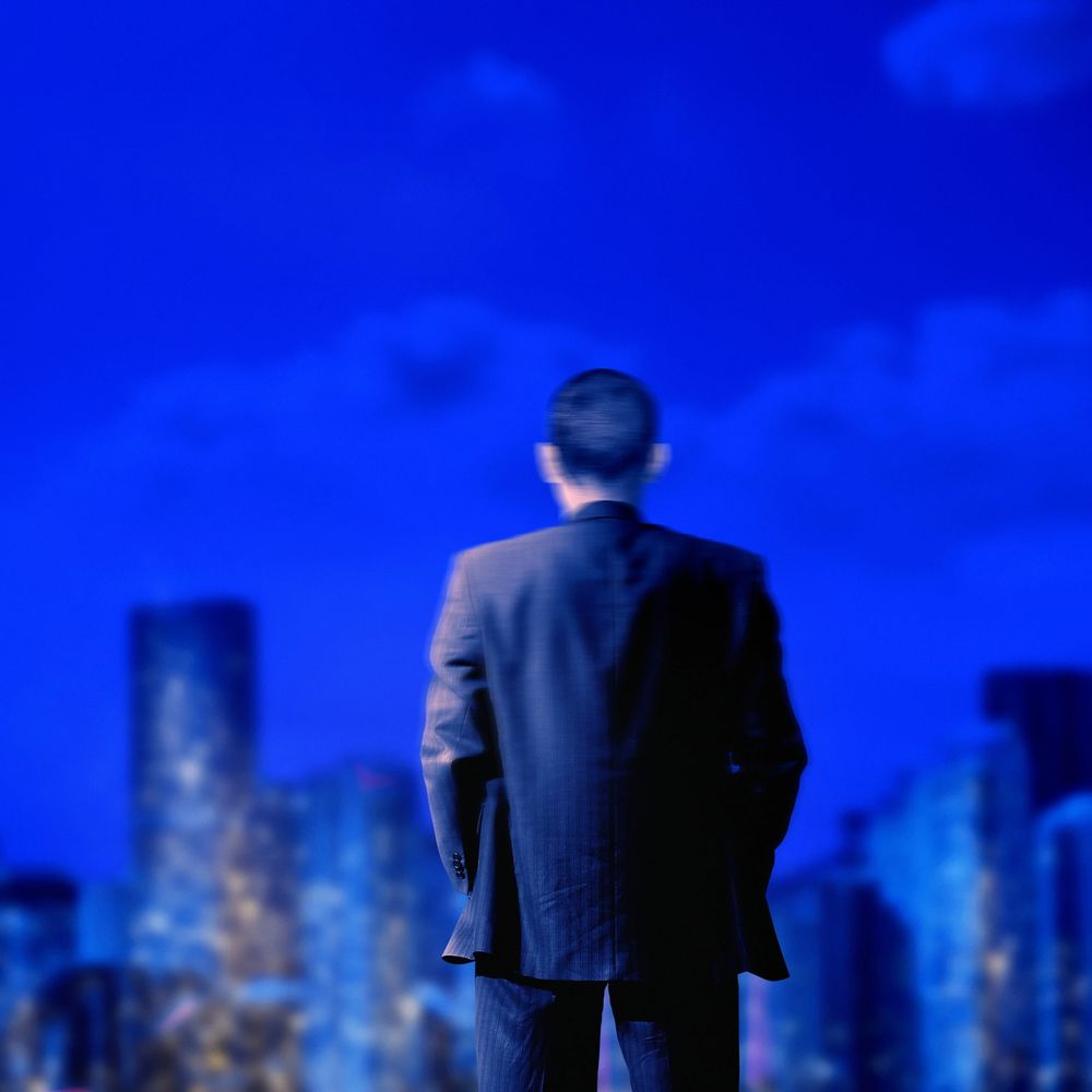 Man in suit looking at city skyline under a deep blue sky.