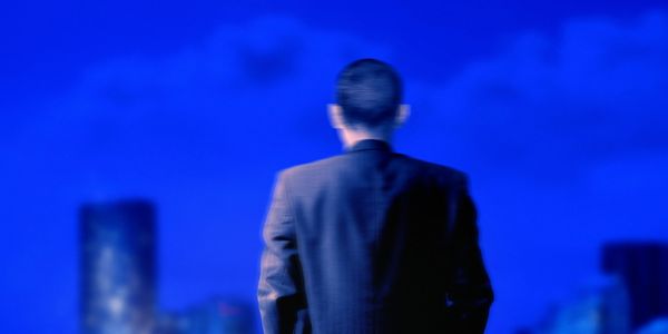 Man in suit looking at city skyline under a deep blue sky.