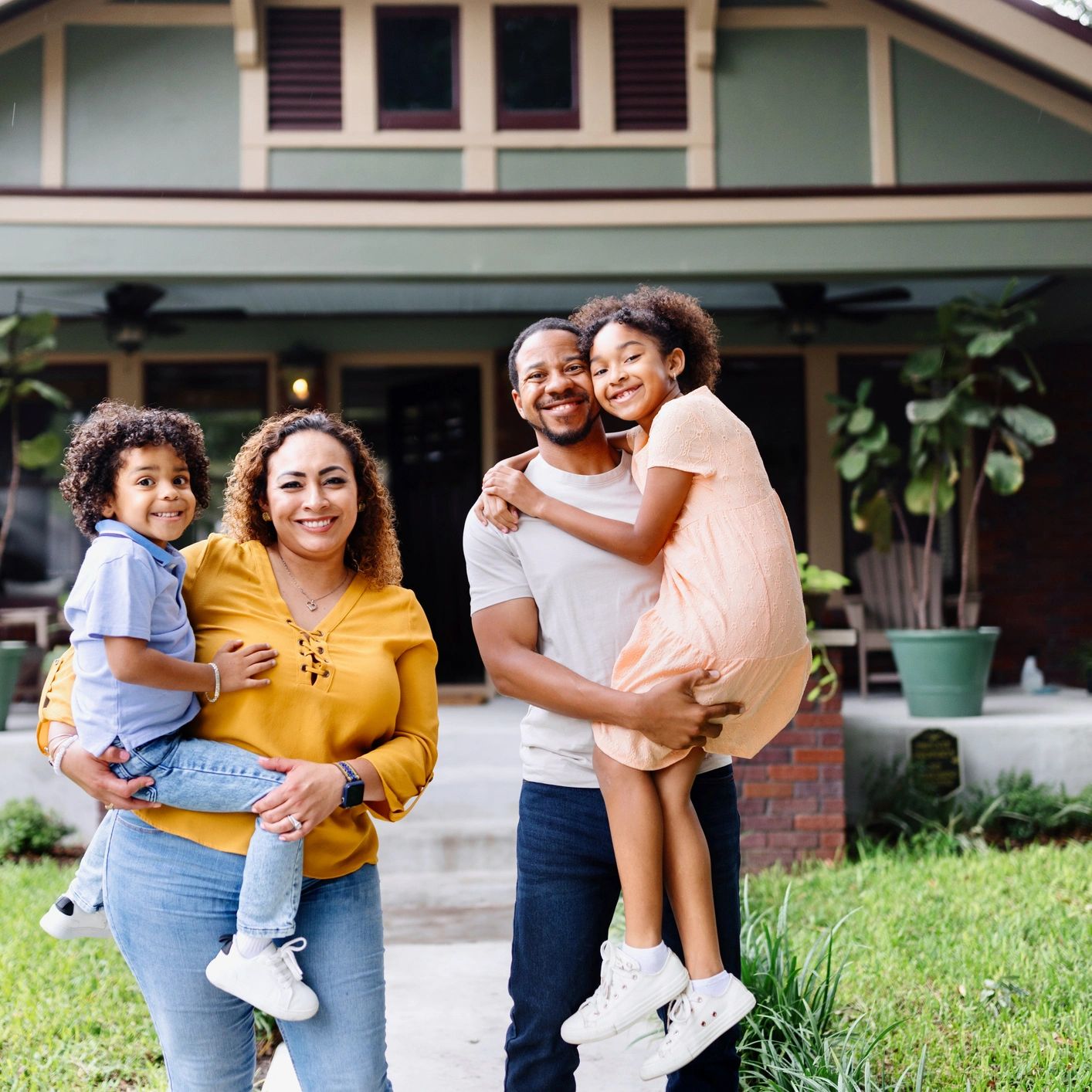 African American couple with children in front of their new home. She is holding their little boy an