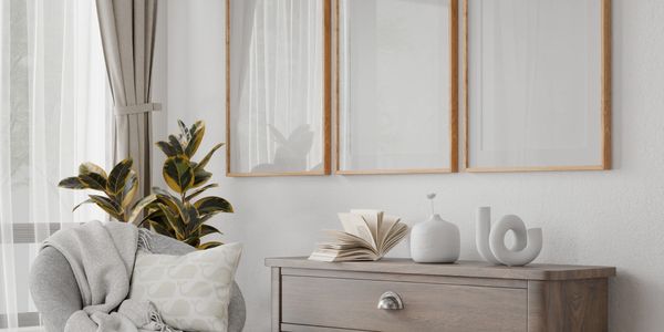 Cozy corner with a chair, soft throw, and wooden dresser under three framed mirrors.