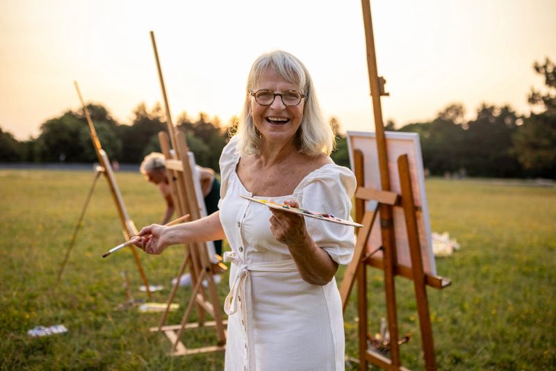 Woman artist painting together with her friends outdoors on a meadow in nature.