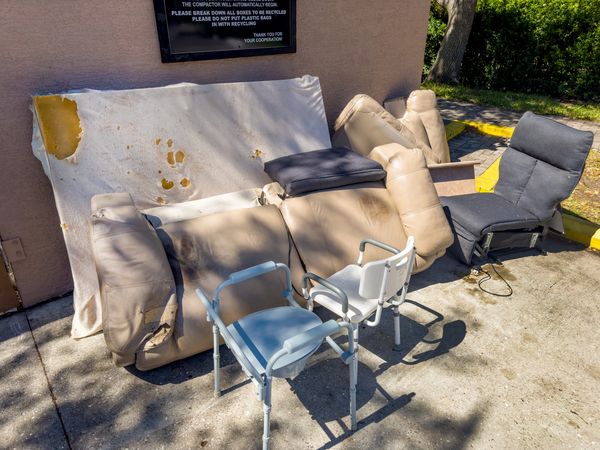 Worn-out furniture and medical chairs left outside near a wall.