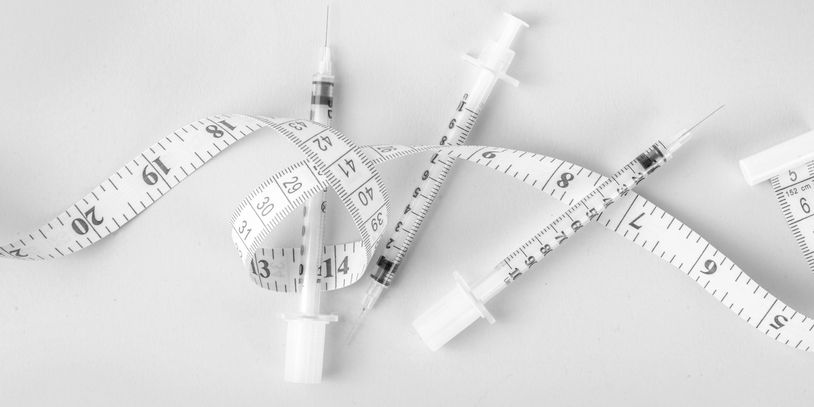 Syringes intertwined with a measuring tape symbolizing health and weight.