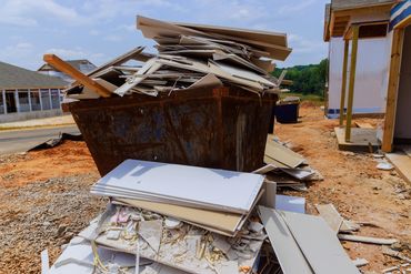 A construction site dumpster overflowing with drywall debris and wood scraps.