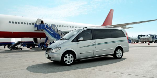 Silver van parked near a large airplane on the tarmac.