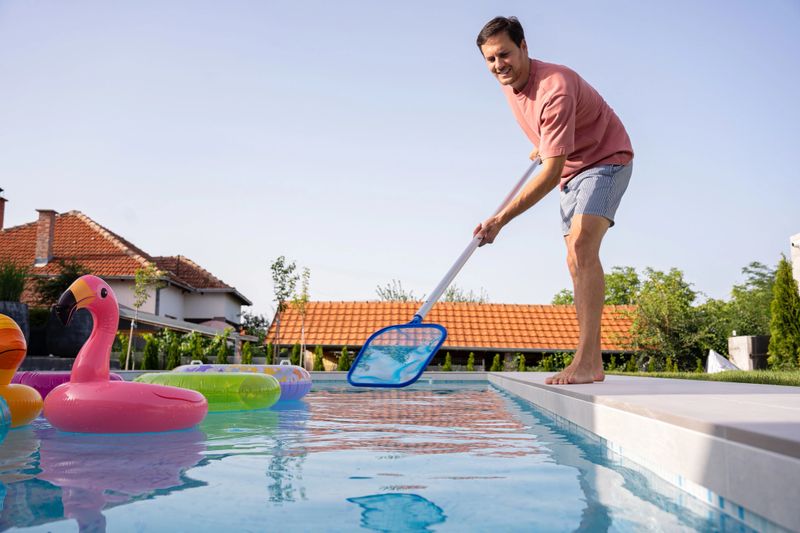 Young man cleaning his swimming pool with a net in the backyard
