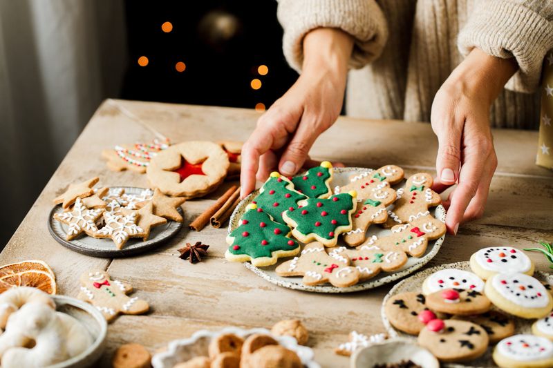 Woman hands arranging sweets on Christmas table. Close-up of female placing homemade gingerbread cookies and sweets on wooden table for Christmas celebration.