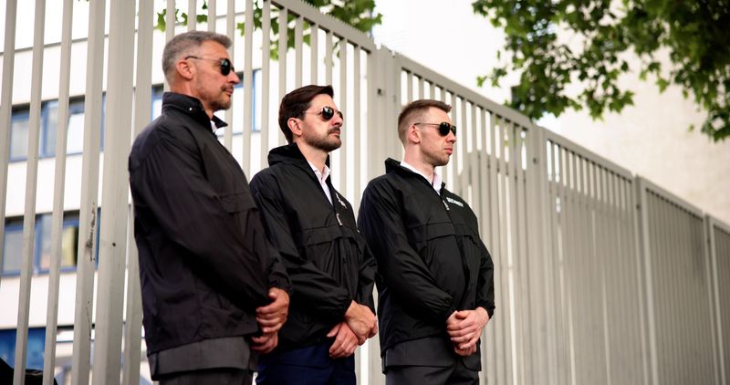 Corporate Security Guard Standing Outside Building Providing Protection for Businessman in Suit â Surveillance Services Offered for VIPs.