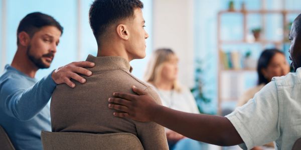 Group therapy session with supportive individuals comforting a young man.