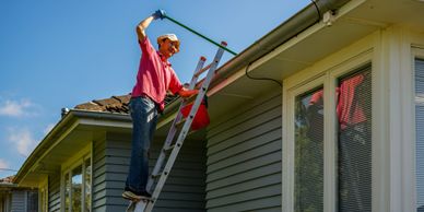 Man cleaning gutters on a roof using a ladder and a tool.