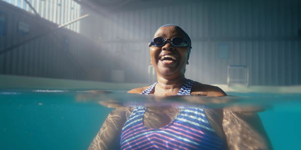 Smiling woman enjoying swimming in a pool, half underwater.