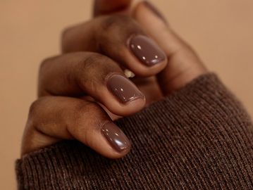 Close-up of hand with glossy brown nails and cozy brown sweater sleeve.