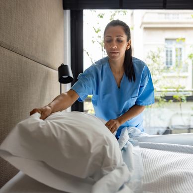 A care assistant is plumping up a pillow after making up a clean bed. 