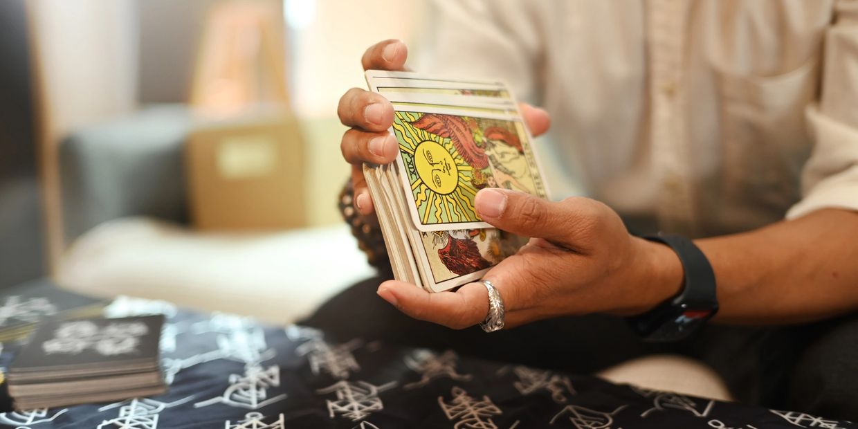 A close up of two hands shuffling a deck of Tarot Cards. The card showing features a big yellow sun.