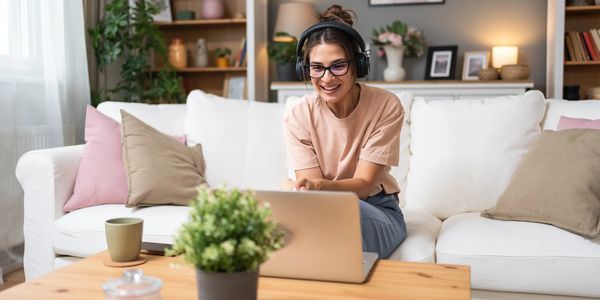 Woman with headphones using laptop on a cozy sofa.