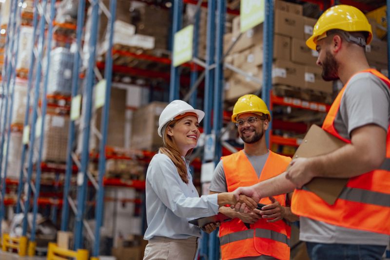 Shot of worker and female manager shaking hands together while standing in a large warehouse