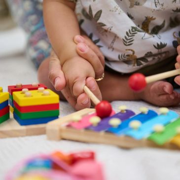Adult helping child play xylophone and build with colorful blocks.