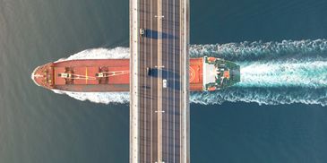 A large ship sails under a bridge with vehicles on it.