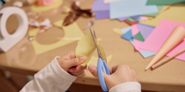 Child cutting yellow paper with blue scissors.