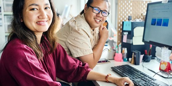 Two colleagues smiling while working at a computer in an office.
