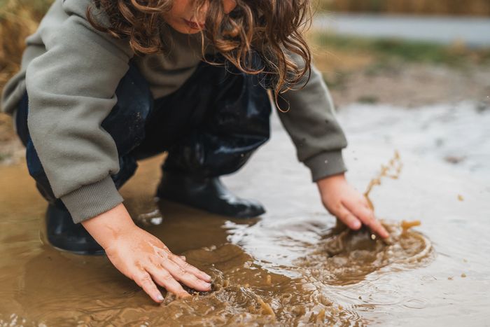 Child playing and splashing in muddy water with hands.