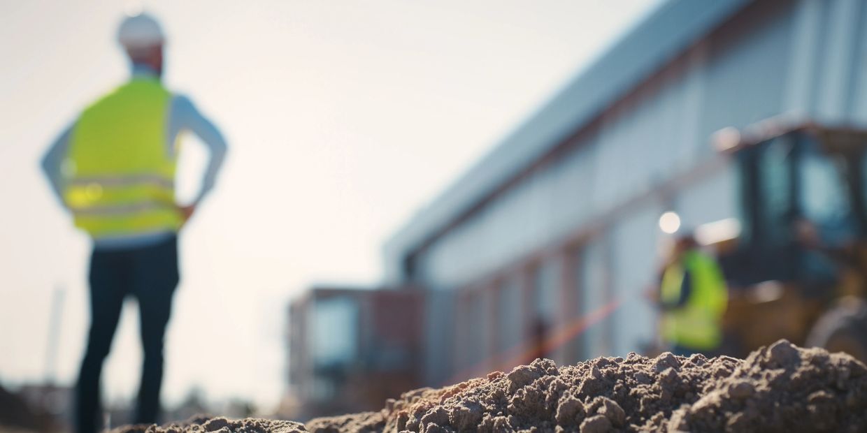 Construction worker in a safety vest overlooking a worksite with dirt in focus.