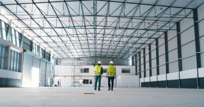 Two construction workers inspect an empty industrial warehouse interior.