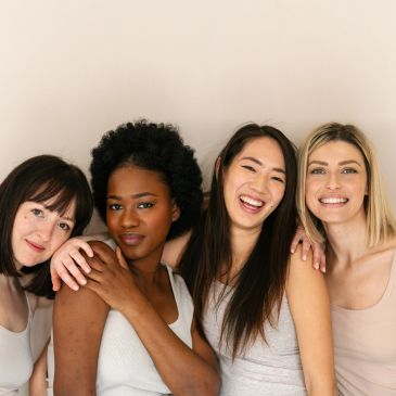 Four diverse women smiling together in neutral tones.