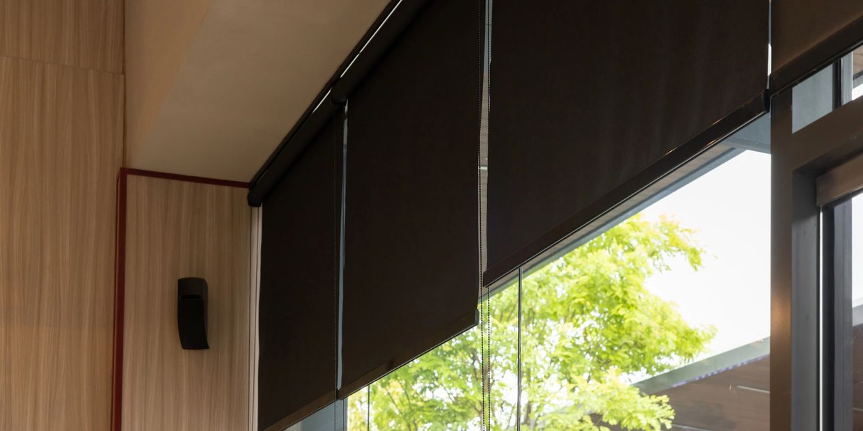Modern window with partially lowered black roller blinds and green trees outside.