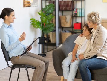 A therapist listens to a concerned mother and child during a counseling session.