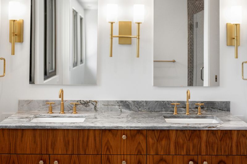This image showcases a modern bathroom vanity featuring dual sinks, a marble countertop, and elegant mirrors, accented by sleek, gold fixtures, creating a sophisticated ambience.