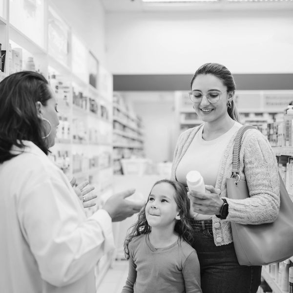 A mother and daughter consult a pharmacist in a drugstore aisle.