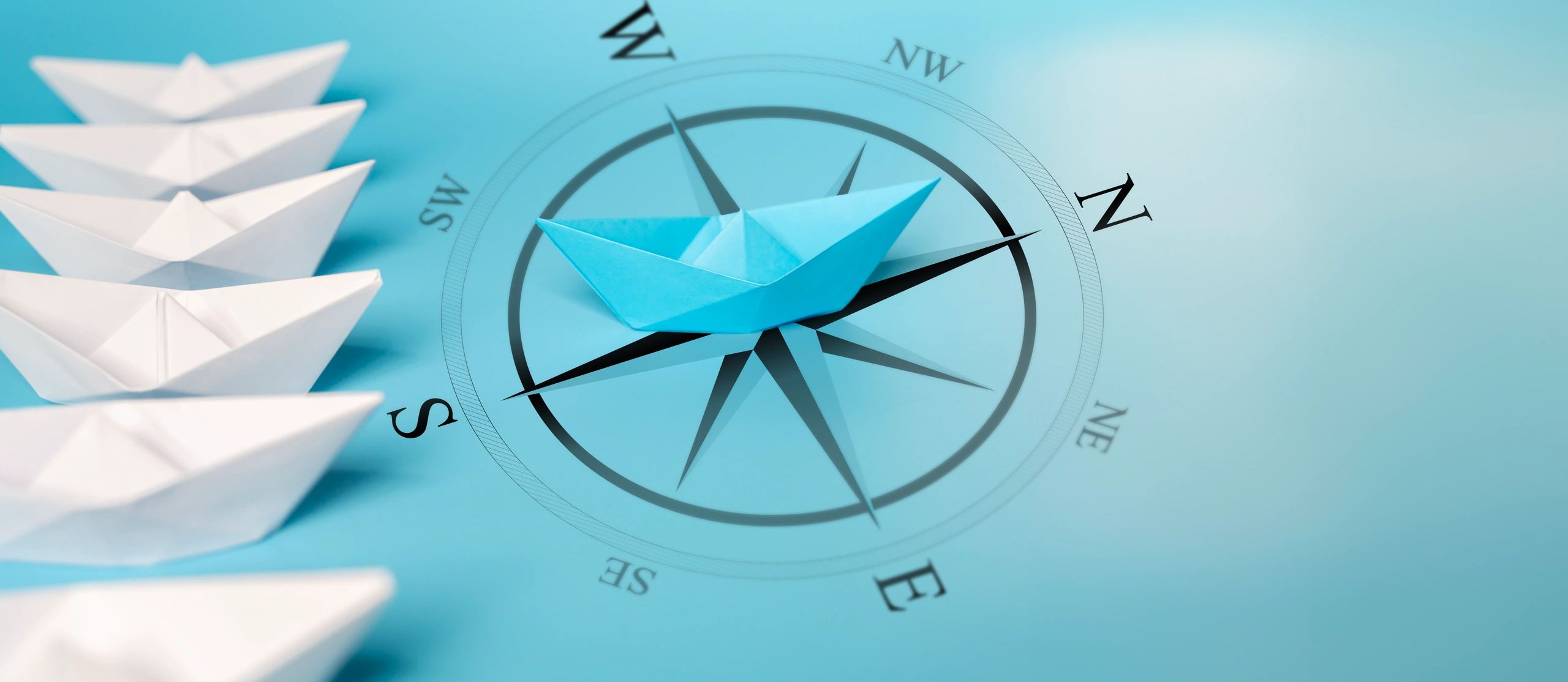 Blue paper boat leading white boats on a compass.