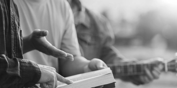 Two people reading and discussing a book, one pointing at the text.