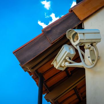 Two security cameras mounted on a building under a clear blue sky.