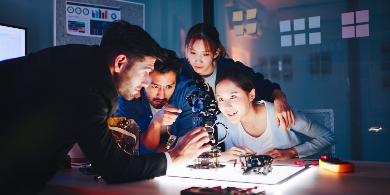 Four young engineers excitedly work on a robotic arm prototype together.