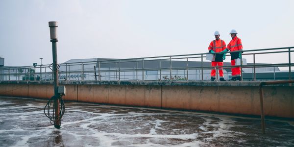 Two workers in orange safety gear at a wastewater treatment plant.