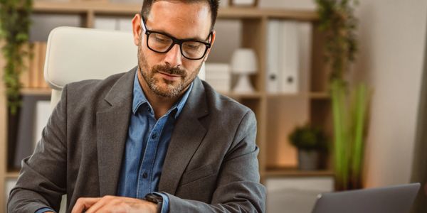 Man in glasses opening a large envelope at his desk.