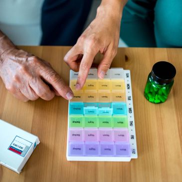 Hands organizing a weekly pill organizer and medicine bottle on a table.