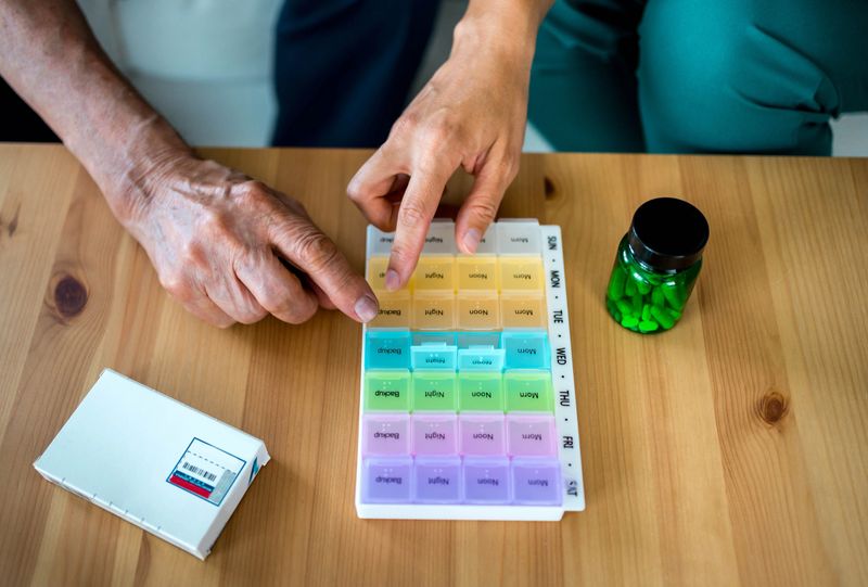 Home nurse helps senior patient to prepare weekly pill organizer