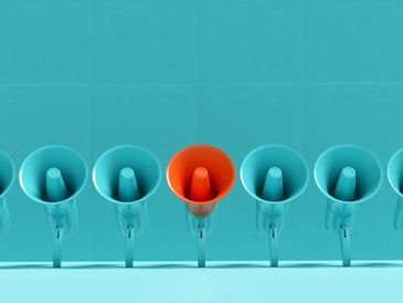 One orange megaphone among several blue megaphones on a turquoise background.