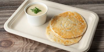 Two fluffy dosas with coconut chutney on a biodegradable tray.