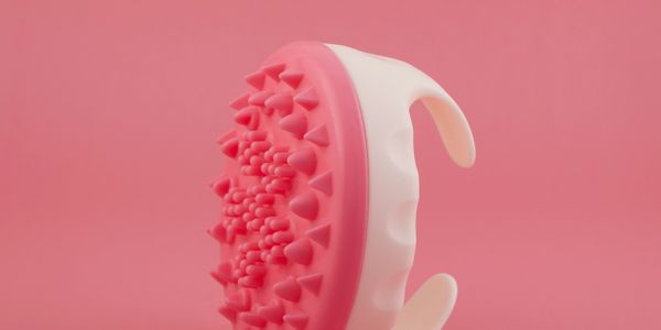 Pink and white silicone scalp massager with spikes on a pink background.