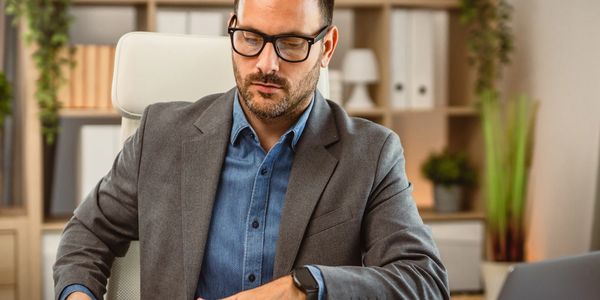A man in glasses and blazer working at a desk in an office.