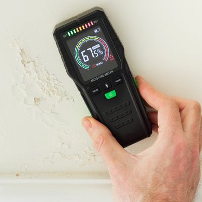 Hand-held moisture meter showing 67.5% moisture on a damaged wall.