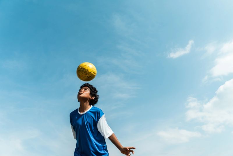 Child boy juggling ball in the soccer field